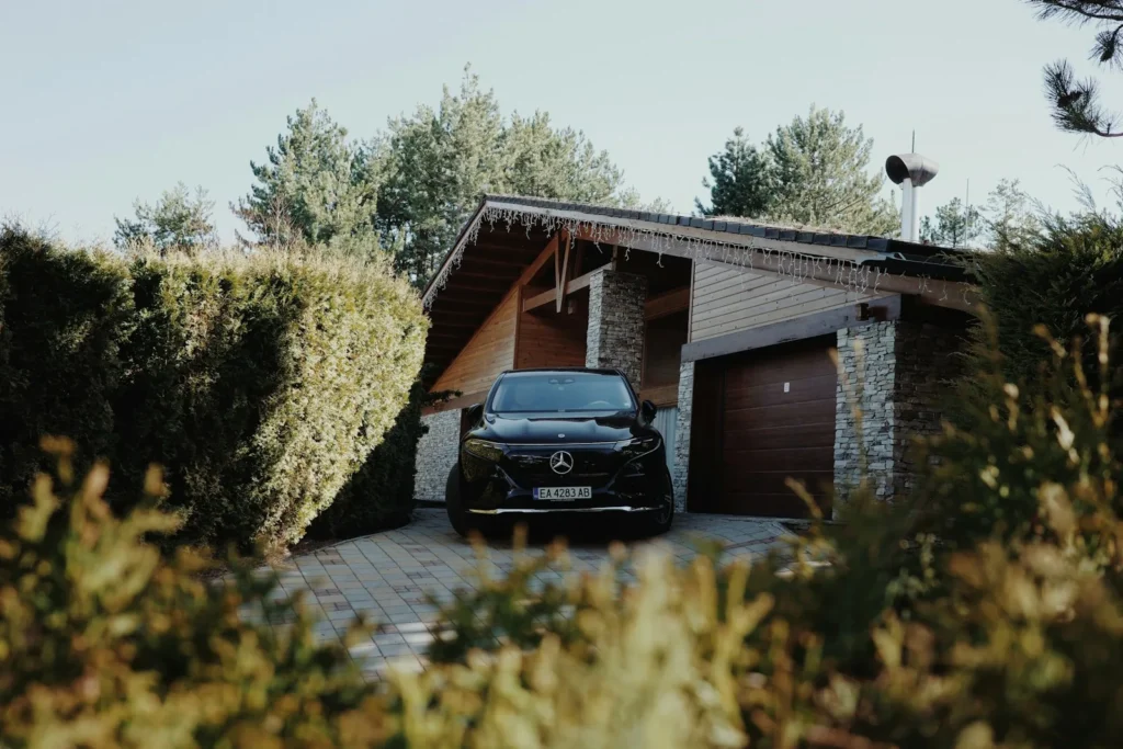 Carport aus Holz mit Satteldach vor einer Garage, darunter ein Auto